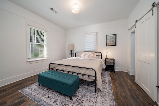 bedroom with a barn door and dark hardwood / wood-style flooring