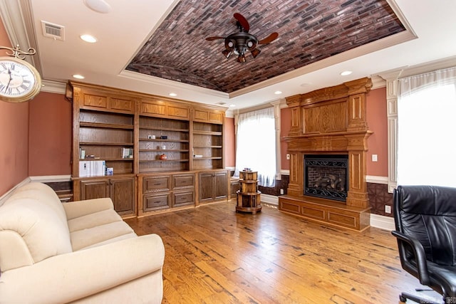 interior space featuring light wood-type flooring, a large fireplace, a tray ceiling, ceiling fan, and crown molding