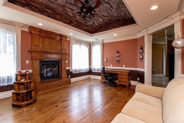 office area featuring ceiling fan, a raised ceiling, hardwood / wood-style flooring, a fireplace, and ornate columns