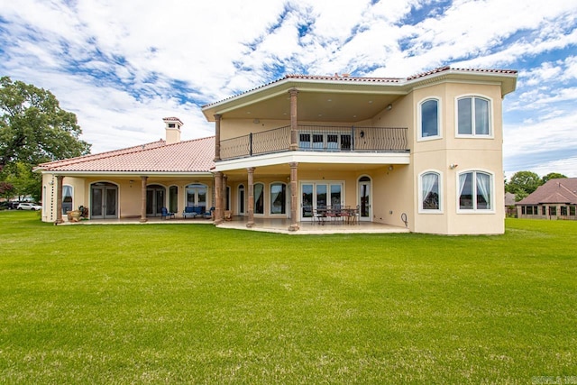 rear view of property featuring a patio area, a yard, and a balcony