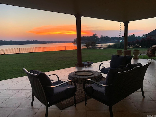 patio terrace at dusk featuring a water view, an outdoor fire pit, and a lawn