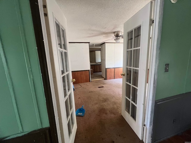 hall with french doors, a textured ceiling, and dark carpet