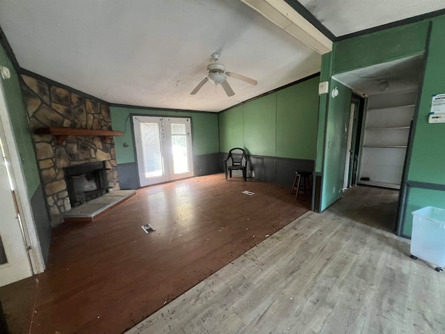 unfurnished living room featuring ceiling fan, a stone fireplace, ornamental molding, and light wood-type flooring