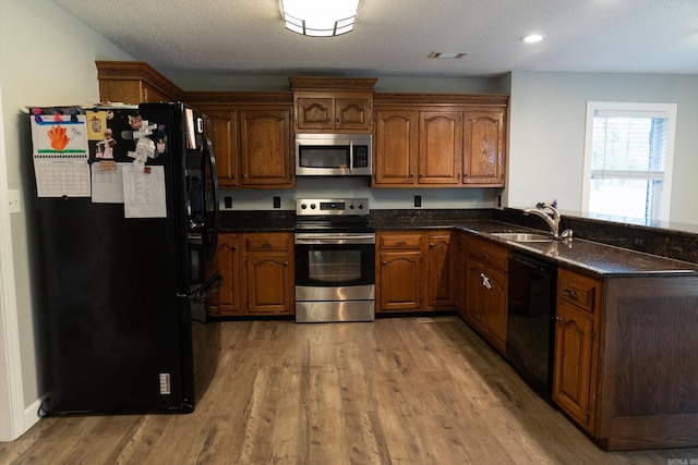 kitchen with dark stone counters, hardwood / wood-style floors, sink, black appliances, and a textured ceiling