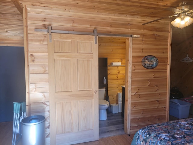 bedroom featuring hardwood / wood-style flooring, wooden walls, wooden ceiling, ensuite bathroom, and ceiling fan