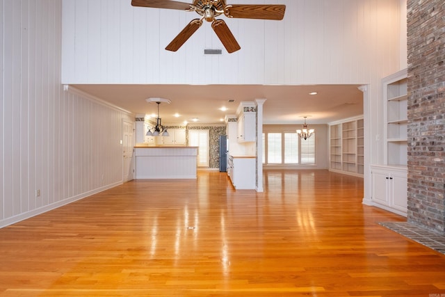 unfurnished living room featuring wooden walls, ceiling fan with notable chandelier, light wood-type flooring, and built in features