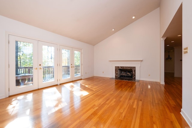 unfurnished living room featuring light hardwood / wood-style floors, french doors, a premium fireplace, and high vaulted ceiling