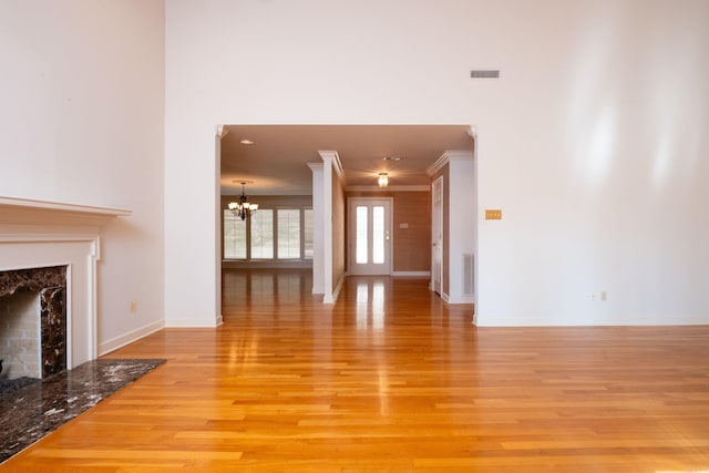 unfurnished living room with ornamental molding, light hardwood / wood-style flooring, a premium fireplace, and a notable chandelier