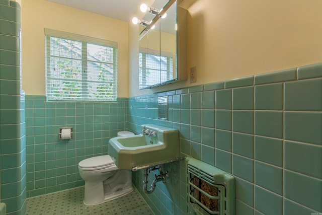 bathroom featuring toilet, heating unit, tile walls, and sink