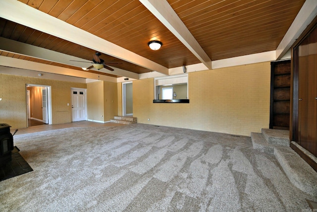 301 Reine St, Mena, AR 71953 - unfurnished living room featuring a wood stove, brick wall, beamed ceiling, ceiling fan, and carpet