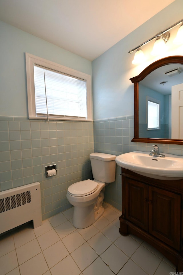 bathroom with a healthy amount of sunlight, radiator heating unit, toilet, tile walls, and vanity