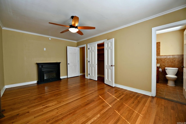 unfurnished bedroom featuring ceiling fan, tile walls, ensuite bathroom, and hardwood / wood-style floors