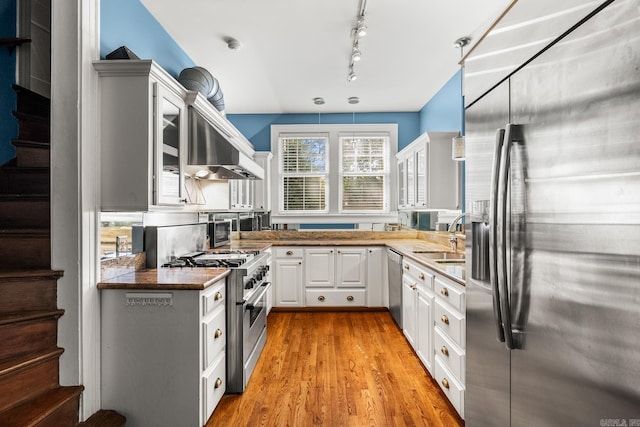 kitchen with wall chimney range hood, sink, white cabinetry, appliances with stainless steel finishes, and light hardwood / wood-style floors