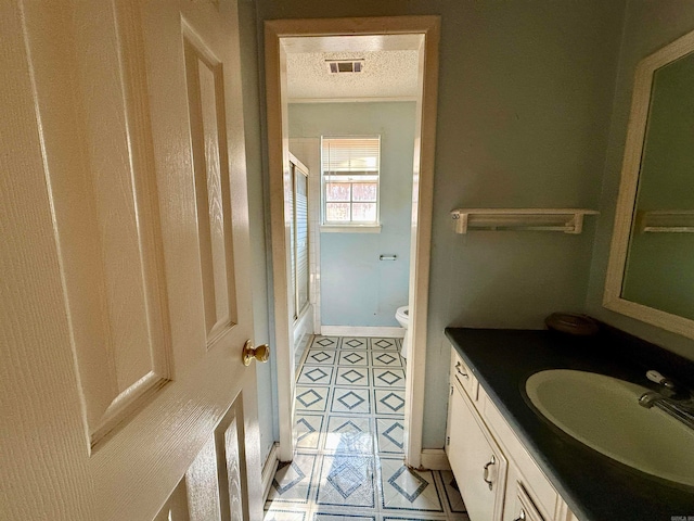 bathroom featuring vanity, toilet, a textured ceiling, and tile patterned flooring