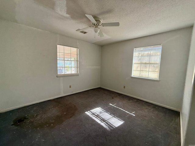 spare room featuring dark carpet, ceiling fan, a textured ceiling, and plenty of natural light