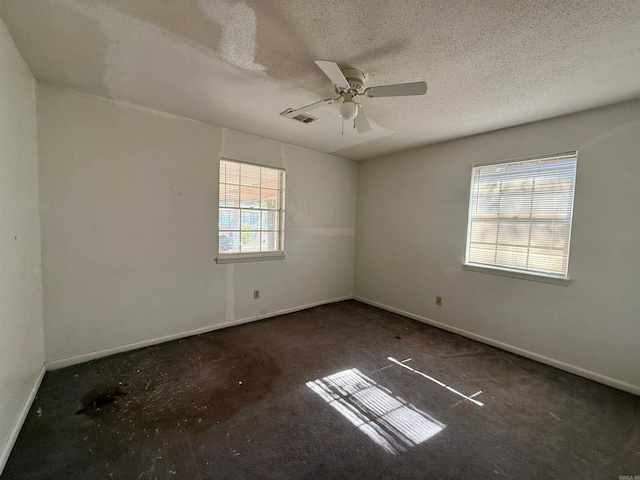 spare room with a textured ceiling, dark carpet, and ceiling fan