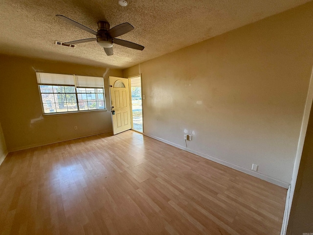 empty room with a textured ceiling, light wood-type flooring, and ceiling fan