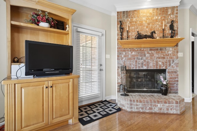 living area with wood finished floors, ornamental molding, baseboards, and a brick fireplace
