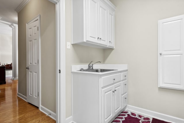 laundry room featuring a sink, light wood finished floors, and baseboards