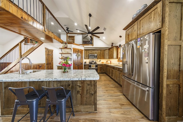 kitchen with light hardwood / wood-style flooring, appliances with stainless steel finishes, light stone counters, high vaulted ceiling, and ceiling fan