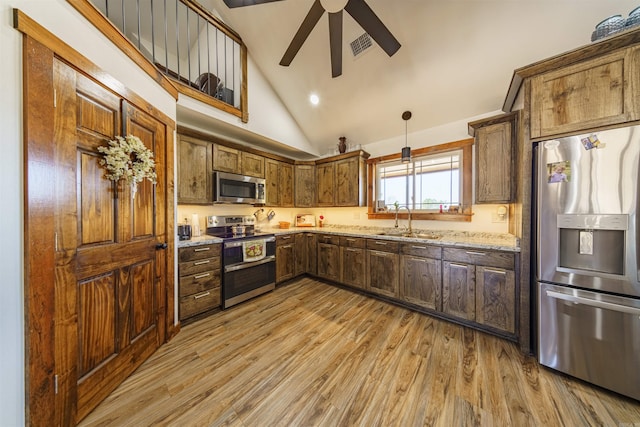 kitchen with stainless steel appliances, sink, light wood-type flooring, and decorative light fixtures