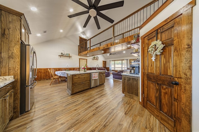 kitchen featuring light stone countertops, appliances with stainless steel finishes, light wood-type flooring, wooden walls, and high vaulted ceiling