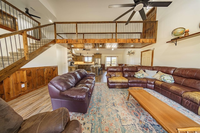 living room featuring light hardwood / wood-style flooring, wooden walls, a high ceiling, and ceiling fan