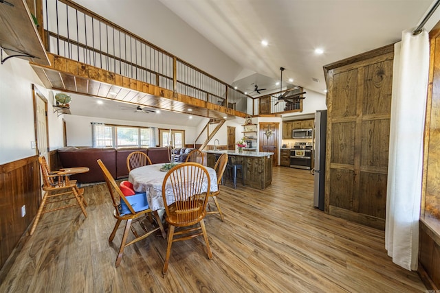 dining room featuring wood walls, wood-type flooring, a high ceiling, and ceiling fan