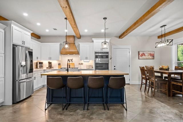 kitchen with a kitchen island with sink, stainless steel appliances, pendant lighting, custom exhaust hood, and white cabinetry