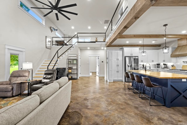 living room featuring beam ceiling, a towering ceiling, sink, and ceiling fan