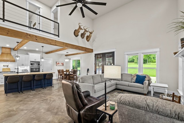 living room with ceiling fan, beamed ceiling, and a high ceiling