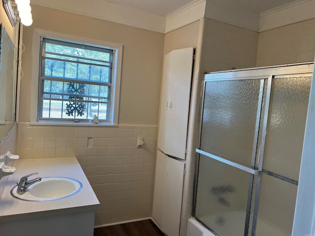 bathroom featuring wood-type flooring, tile walls, bath / shower combo with glass door, vanity, and crown molding