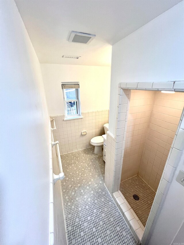 bathroom with tile walls, a tile shower, toilet, and tile patterned floors