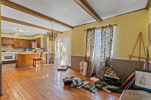 dining space with wooden walls, ceiling fan with notable chandelier, a textured ceiling, and light wood-type flooring