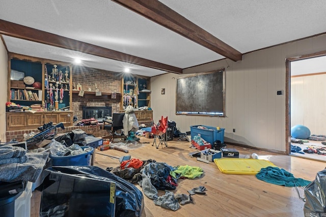 living room featuring beam ceiling, a textured ceiling, wood-type flooring, wood walls, and a fireplace