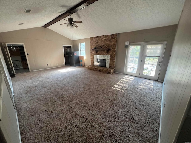 unfurnished living room featuring carpet flooring, lofted ceiling with beams, a brick fireplace, ceiling fan, and wooden walls