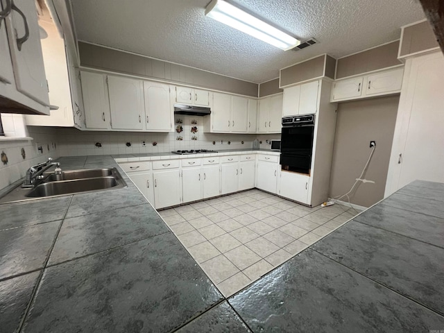 kitchen featuring white cabinets, tasteful backsplash, light tile patterned floors, stainless steel gas stovetop, and sink