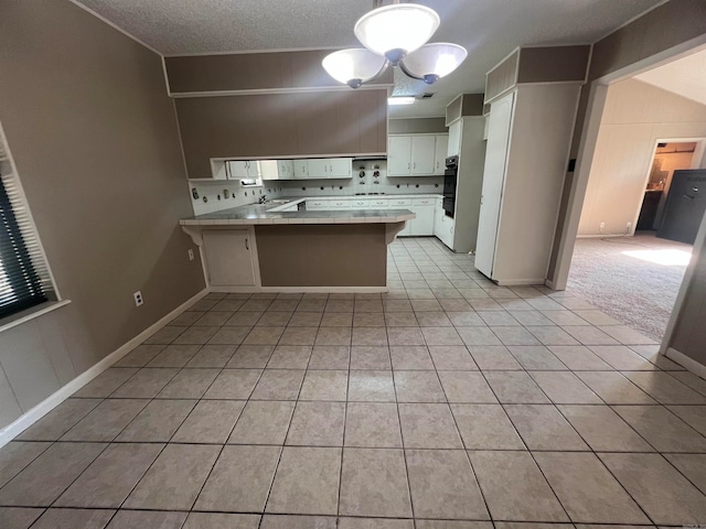 kitchen featuring kitchen peninsula, white cabinets, hanging light fixtures, a kitchen breakfast bar, and a textured ceiling