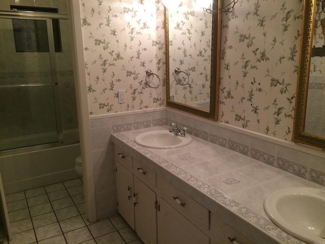 full bathroom with combined bath / shower with glass door, tile walls, toilet, vanity, and tile patterned flooring