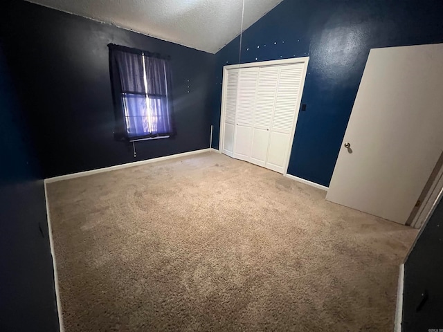 unfurnished bedroom featuring a closet, a textured ceiling, carpet flooring, and lofted ceiling