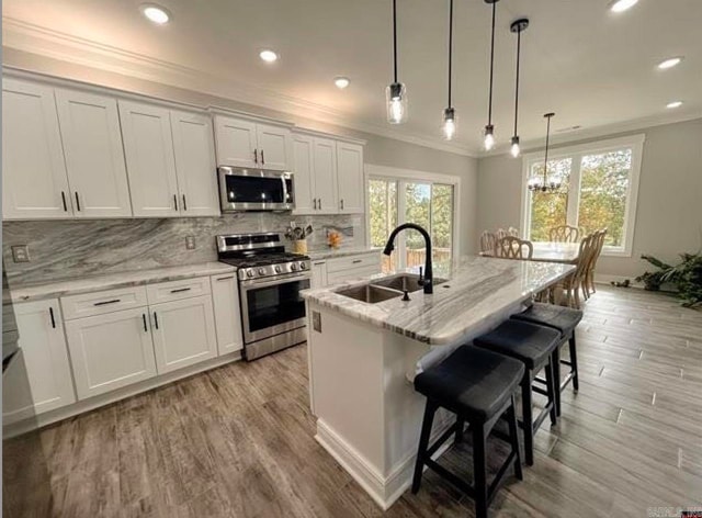 kitchen featuring a breakfast bar area, a center island with sink, sink, white cabinetry, and appliances with stainless steel finishes