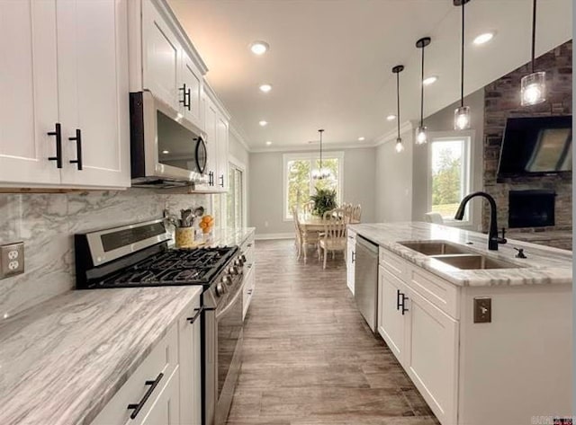 kitchen with appliances with stainless steel finishes, white cabinetry, sink, and hanging light fixtures