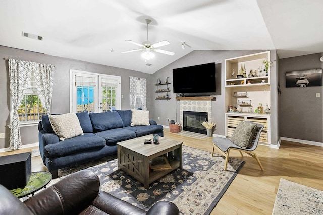 living room featuring lofted ceiling, a tiled fireplace, light wood-type flooring, and ceiling fan