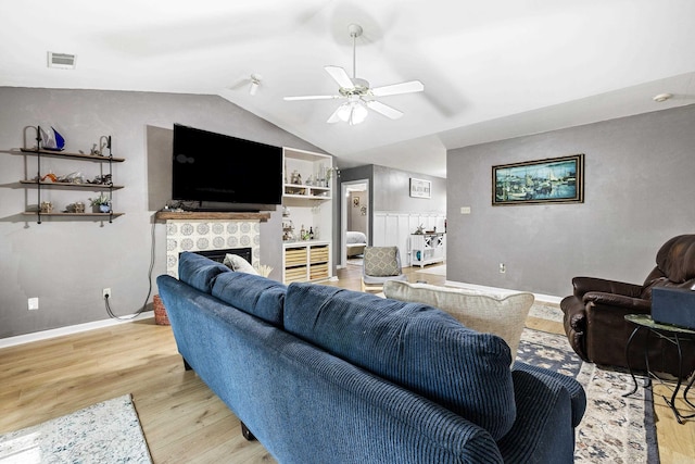 living room featuring a tiled fireplace, vaulted ceiling, light hardwood / wood-style flooring, and ceiling fan