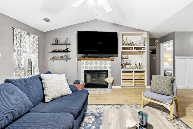 living room with ceiling fan, a tile fireplace, light wood-type flooring, and vaulted ceiling