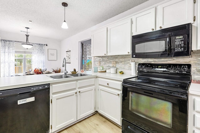 kitchen with black appliances, sink, hanging light fixtures, white cabinetry, and light hardwood / wood-style flooring