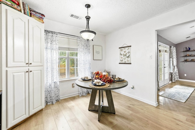 dining area with lofted ceiling, a textured ceiling, and light wood-type flooring