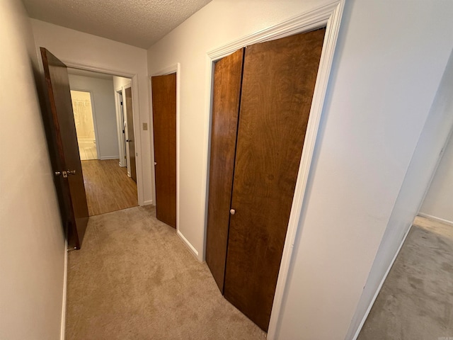 corridor with a textured ceiling and light colored carpet