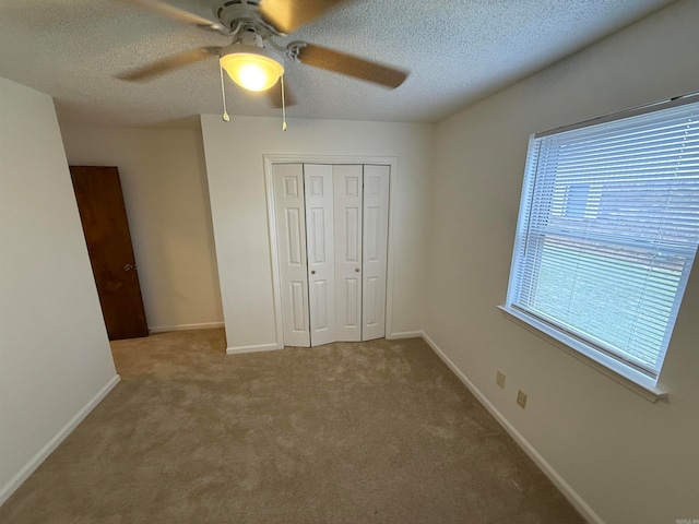 unfurnished bedroom with a textured ceiling, carpet flooring, a closet, and ceiling fan