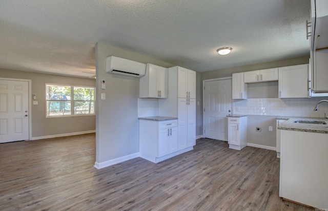 kitchen with a wall unit AC, light stone countertops, white cabinets, light hardwood / wood-style floors, and tasteful backsplash